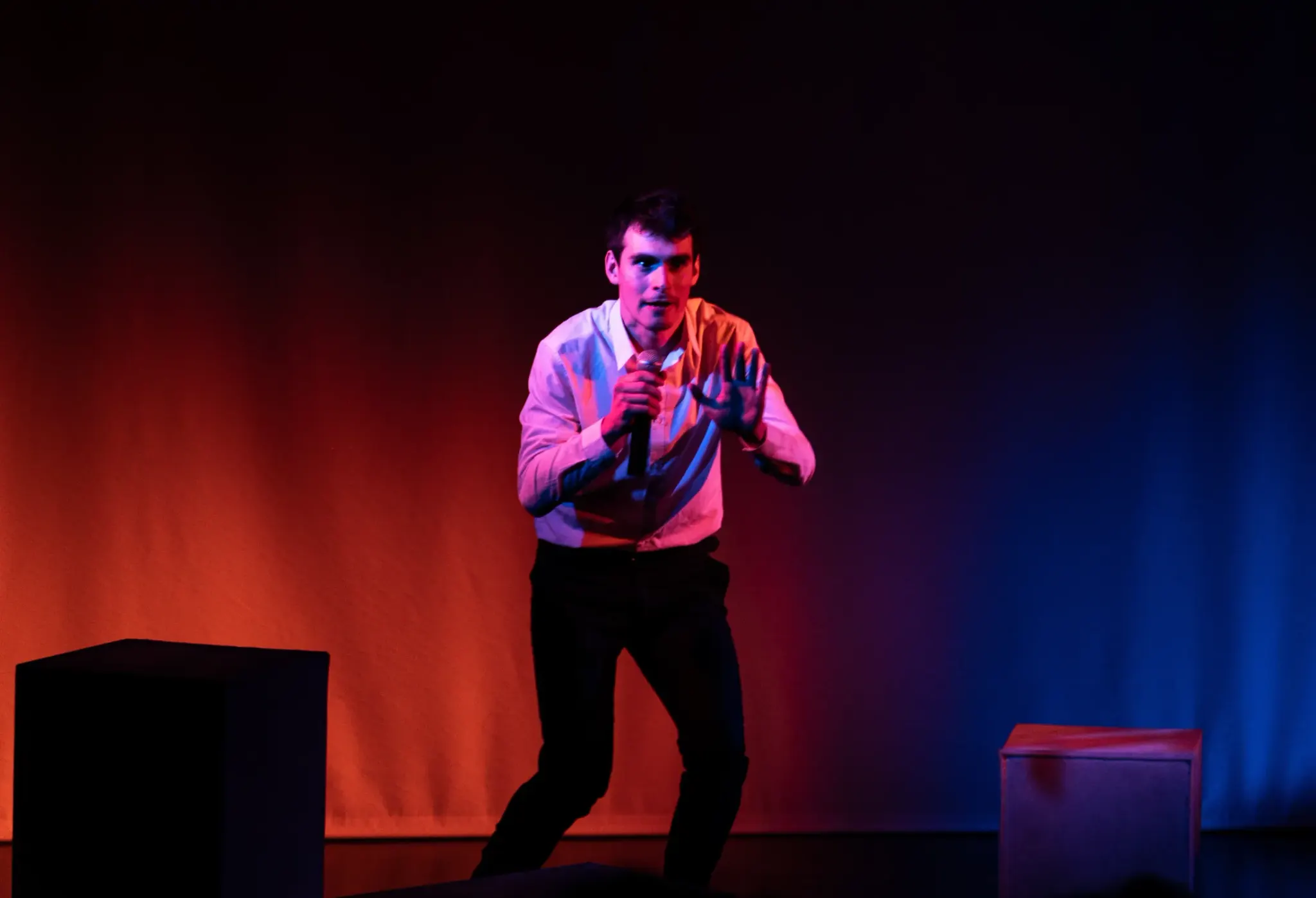 Léo Barcet sur scène, micro en main, dans une lumière orange et bleue